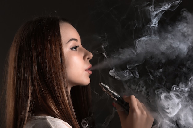 El rostro de una mujer joven vaping en el estudio negro