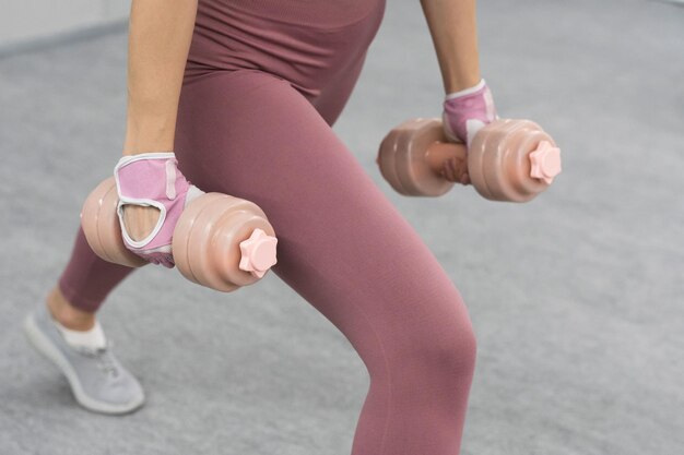 Sin rostro visible Mujer joven atlética haciendo levantamiento pesado usando pesas en el gimnasio