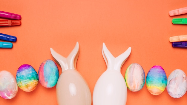 Foto gratuita rotuladores de colores y huevos de pascua sobre un fondo naranja