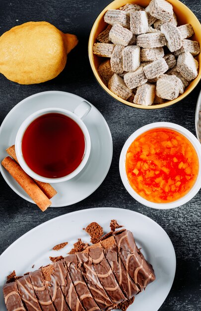 Roulade en rodajas en platos con té, gofres y gelatina, vista de ángulo alto sobre una textura oscura