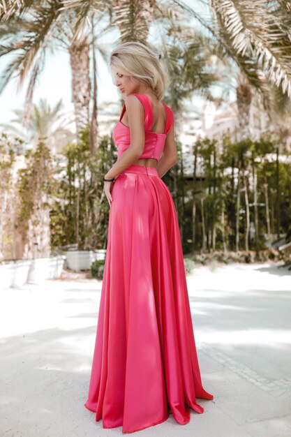 Rubia bien formada junto al mar en Dubai, palmeras, vestidos hermosos y calientes, sesión de fotos de moda de estilo de vida soleado de verano, vestido ondeando en el viento, tranquilo y relajado cerca de la piscina, peinado, maquillaje