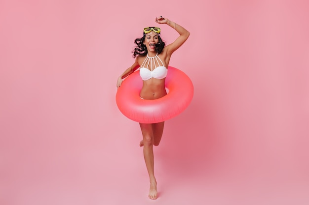 Rubia dama delgada en bikini bailando sobre fondo rosa