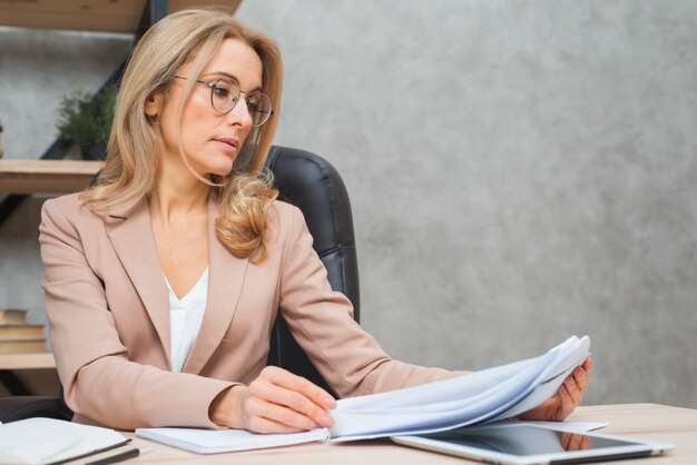 Rubia joven empresaria leyendo los documentos en el lugar de trabajo