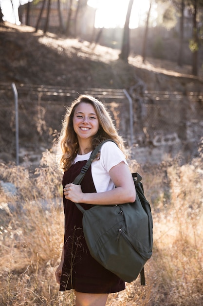 Foto gratuita rubia con mochila sonriendo y mirando a cámara