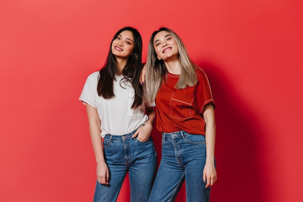 Rubia y morena posando sobre fondo rojo Las mujeres en camisetas simples están sonriendo