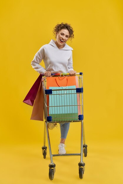 Rubia con pelo rizado conduciendo carrito de compras