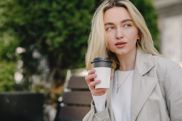 Rubia sentada en un banco con una taza de papel