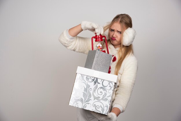 Rubia en suéter blanco tomando regalo de caja blanca.