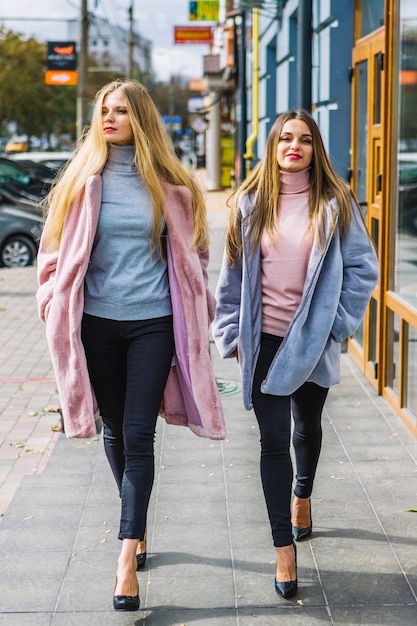 Rubias mujeres jóvenes con las manos en el bolsillo caminando en la calle