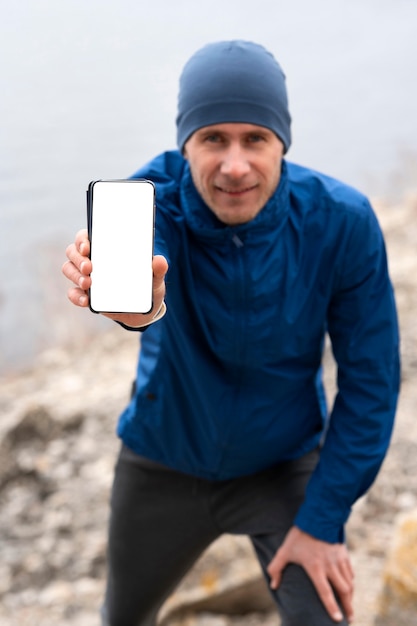 Runner mostrando teléfono en blanco en la naturaleza