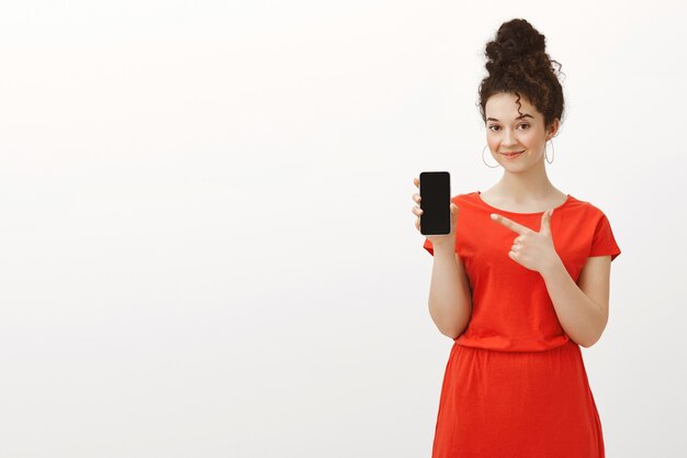 Sabes qué gadget compra a continuación. Retrato de coqueta compañera de trabajo guapa en elegante vestido rojo con pelo rizado peinado en moño