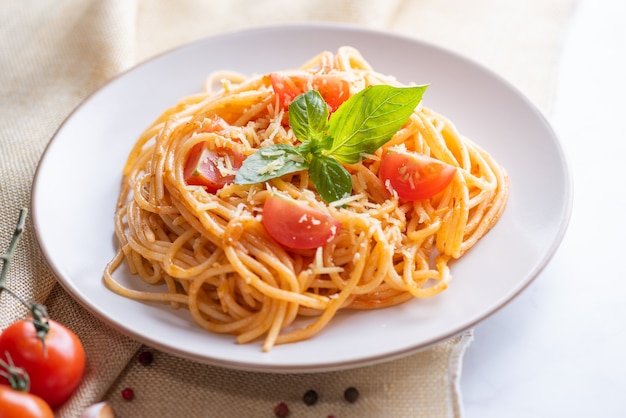 Sabrosa y apetitosa pasta de espagueti italiano clásico con salsa de tomate, queso parmesano y albahaca en un plato e ingredientes para cocinar pasta en la mesa de mármol blanco.