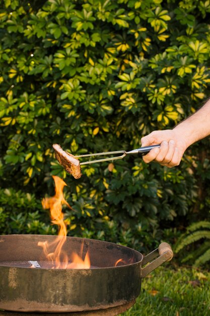 Sabrosa carne a la brasa en pinzas de metal en las manos.