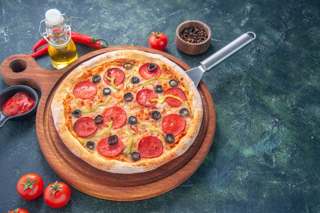 Sabrosa pizza casera sobre tablero de madera, botella de aceite, tomates, pimienta sobre superficie oscura