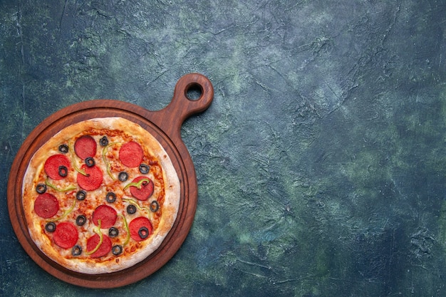 Sabrosa pizza en tabla de cortar de madera en el lado derecho sobre superficie azul oscuro con espacio libre