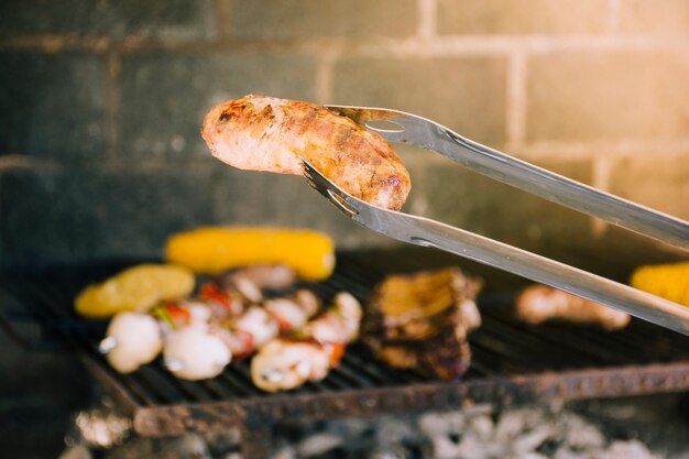 Sabrosa salchicha a la parrilla en pinzas de metal.