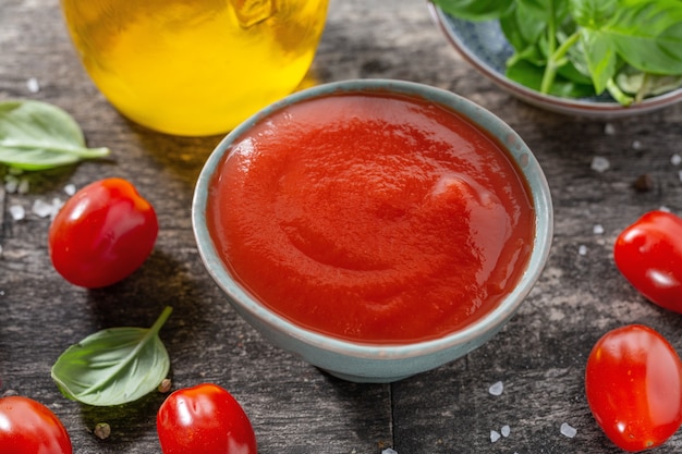 Sabrosa salsa de tomate fresco en un tazón pequeño con ingredientes para cocinar sobre fondo de madera vieja. De cerca