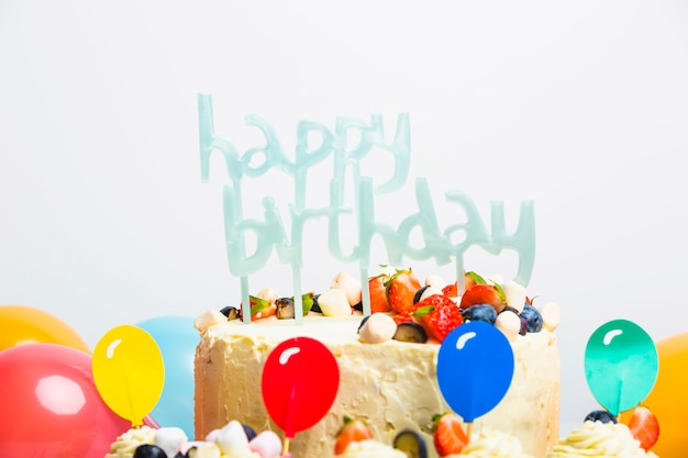 Sabrosa tarta fresca con frutos rojos y título de feliz cumpleaños cerca de un juego de globos