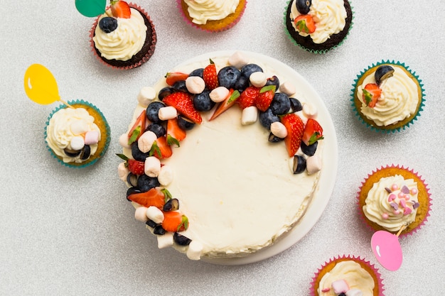 Foto gratuita sabrosa torta fresca con bayas y conjunto de pequeños muffins en mesa