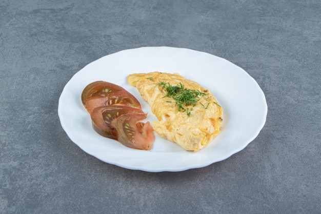 Sabrosa tortilla y rodajas de tomate en la placa blanca.