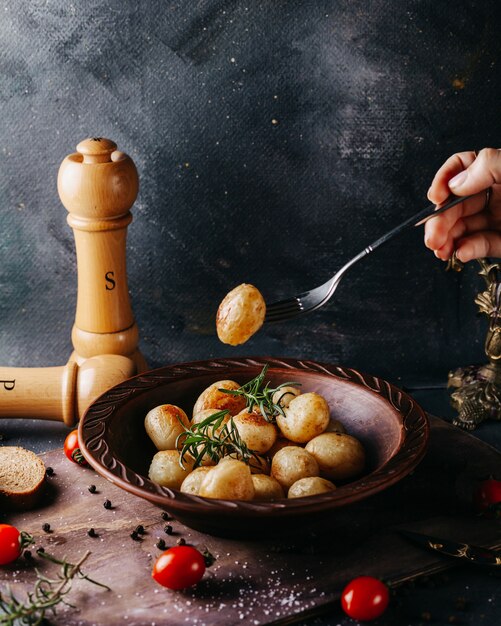 Sabrosas papas enteras cocidas, saladas y condimentadas alrededor de tomates rojos frescos en la superficie oscura