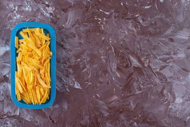 Sabrosas patatas fritas en una placa de madera, sobre la mesa de mármol.