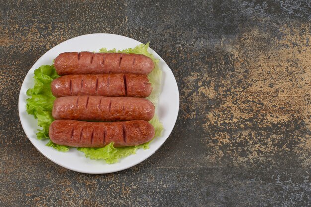 Sabrosas salchichas asadas con lechuga en un plato blanco.