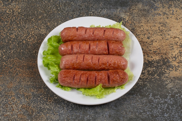 Sabrosas salchichas asadas con lechuga en un plato blanco.