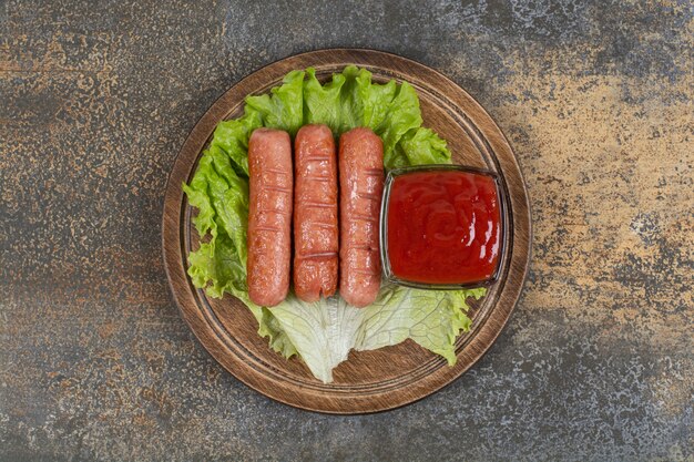 Sabrosas salchichas asadas y salsa de tomate sobre tabla de madera.