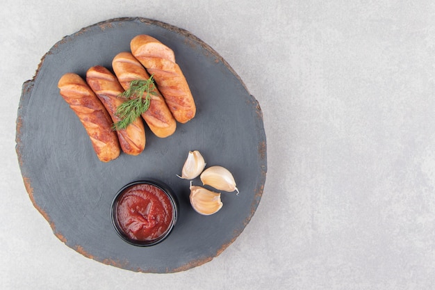 Sabrosas salchichas fritas, ajo y salsa de tomate en pieza de madera.