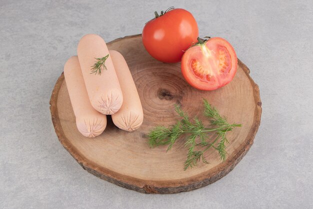 Sabrosas salchichas hervidas y tomates en trozo de madera.