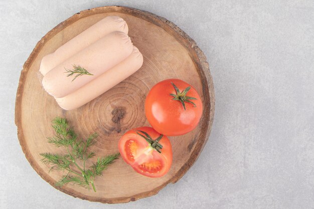 Sabrosas salchichas hervidas y tomates en trozo de madera.