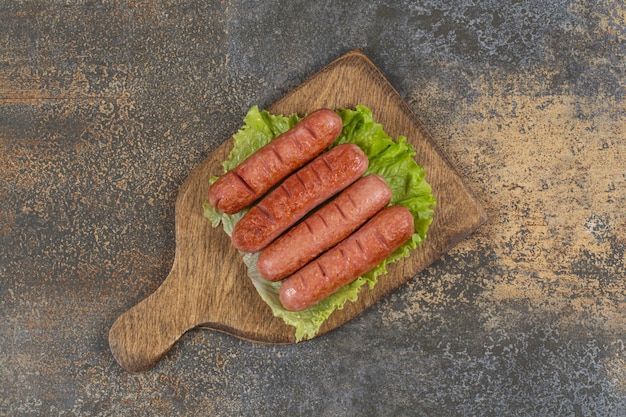 Sabrosas salchichas a la parrilla sobre tabla de madera.