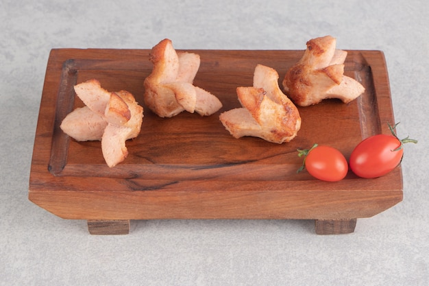 Sabrosas salchichas a la parrilla con tomates sobre tabla de madera.