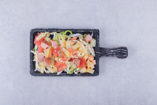 Sabrosas salchichas en rodajas con ensalada fresca en tablero negro.