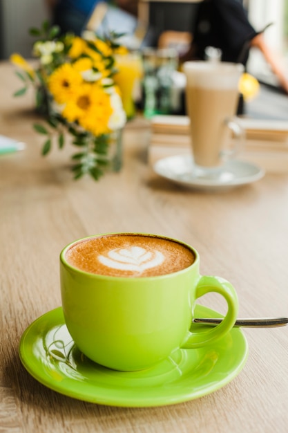 Sabroso café con leche con latte art en taza verde en el restaurante