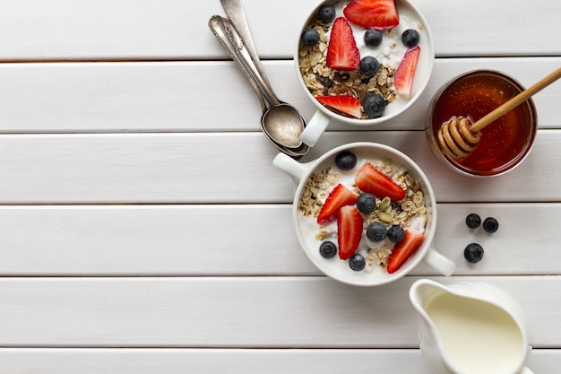 Sabroso desayuno colorido con harina de avena, yogur, fresa, arándano, miel y leche en blanco Fondo de madera con espacio de copia. Vista superior.