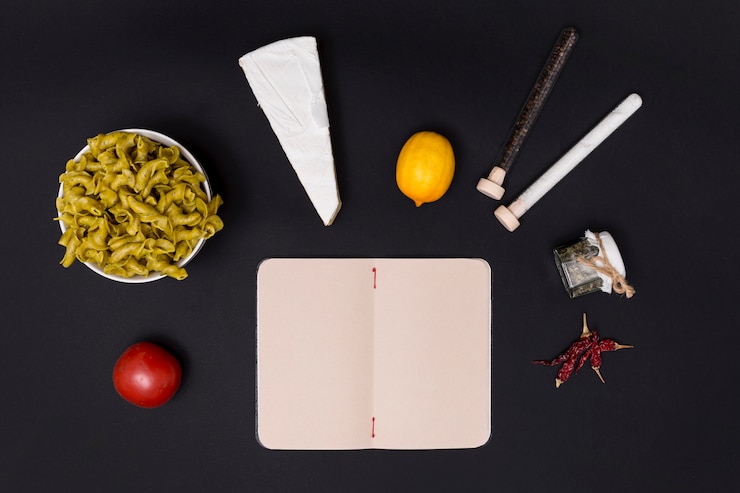 Foto gratuito sabroso ingrediente para hacer pasta con diario abierto en blanco sobre superficie negra
