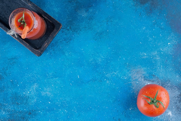 Sabroso jugo de tomate y tomate sobre fondo azul. Foto de alta calidad