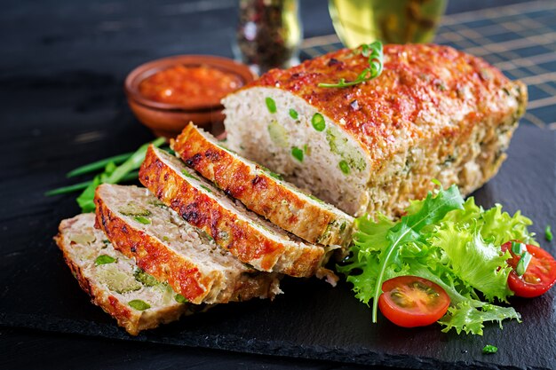 Sabroso pastel de carne de pollo al horno molido casero con guisantes verdes y brócoli en mesa negra.