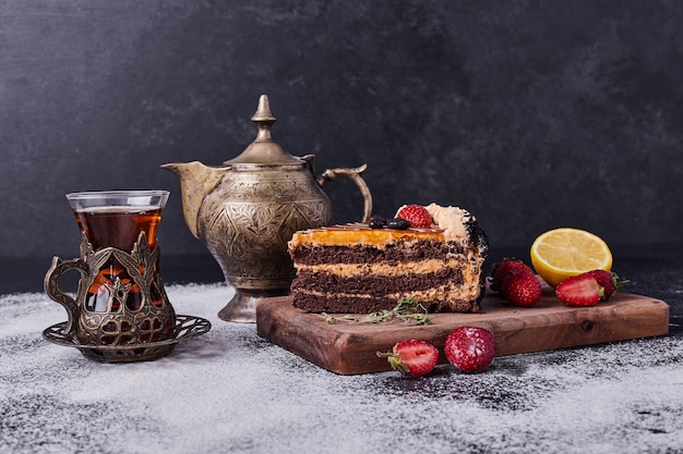 Sabroso pastel de chocolate con juego de té y frutas sobre fondo oscuro.