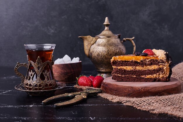 Sabroso pastel de chocolate con juego de té sobre fondo oscuro.