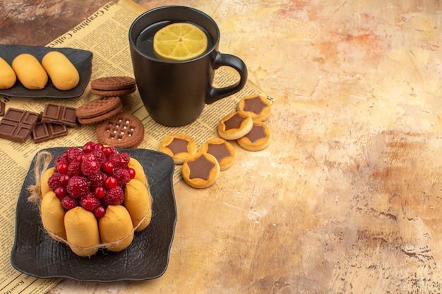 Sabroso pastel de diferentes galletas y té en una taza negra sobre una mesa de colores mezclados