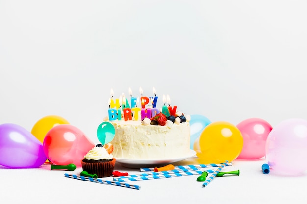 Sabroso pastel con frutos rojos y título de feliz cumpleaños cerca de globos de colores