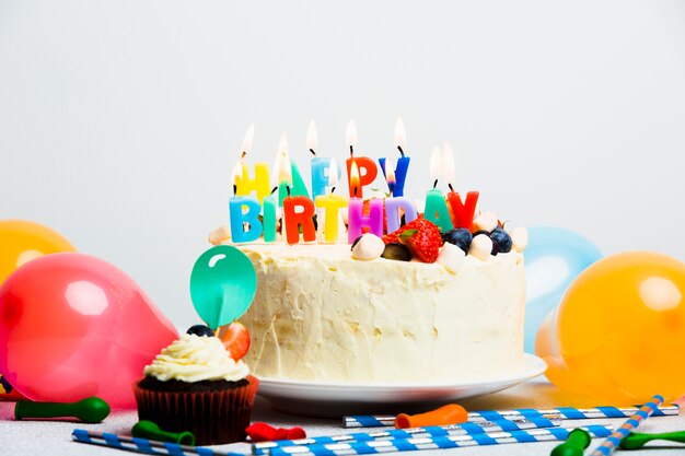 Sabroso pastel con frutos rojos y título de feliz cumpleaños cerca de globos