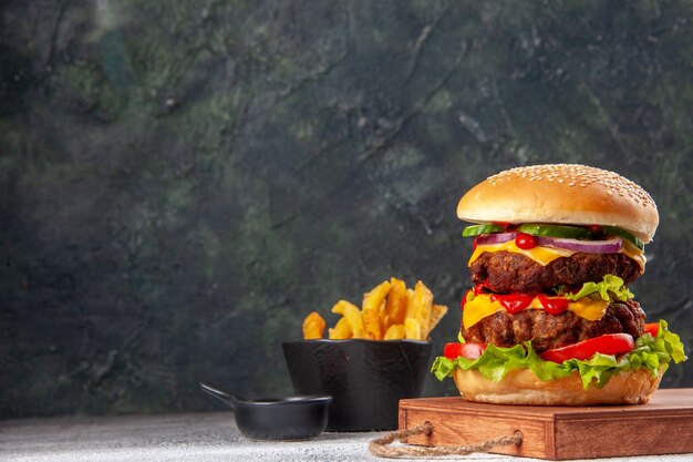 Sabroso sándwich casero en tabla de cortar de madera papas fritas en el lado izquierdo en la superficie borrosa