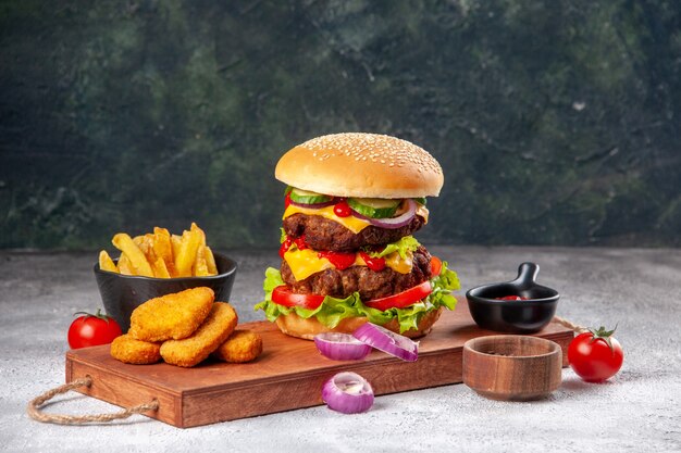 Sabroso sándwich casero y tomates nuggets de pollo cebollas pimiento sobre tabla de cortar de madera papas fritas con salsa de tomate en superficie borrosa