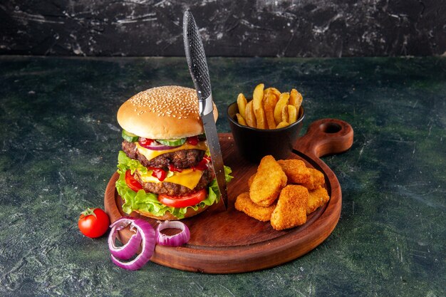 Sabroso sándwich casero tomates pimiento sobre tabla de cortar de madera cebollas tomate con tallo nuggets de pollo papas fritas tenedor sobre superficie de color oscuro