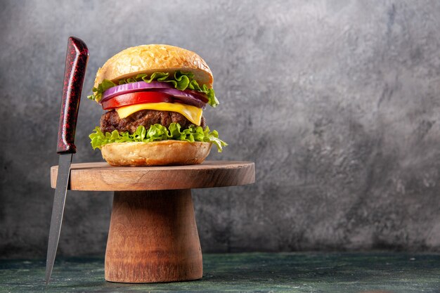Sabroso sándwich y tenedor rojo sobre tabla de cortar de madera en la superficie de color mezcla oscura