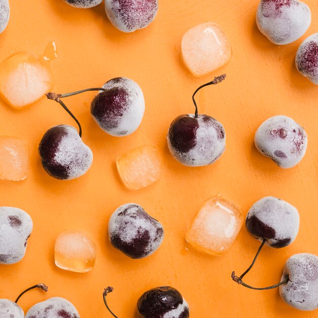 Sabrosos cubitos de cereza y hielo sobre fondo naranja